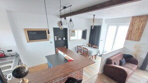Une cuisine moderne avec un mur de fond en briques, un coin repas avec une table et des chaises, et un salon avec un canapé et une plante.