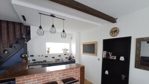 Une cuisine avec un îlot central en briques, des suspensions lumineuses, une porte noire et une bibliothèque.