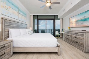 Quarto com cama, escrivaninha, cadeira, ventoinha no teto e varanda com vista.