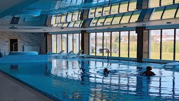 Ein überdachter Swimmingpool mit großen Glaswänden, einem Boden aus Marmorplatten und Blick ins Freie.