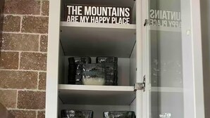 A kitchen cabinet with a sign reading "THE MOUNTAINS ARE MY HAPPY PLACE" and various glass bowls and jars inside. - Our Shangri La (Berkeley Springs)