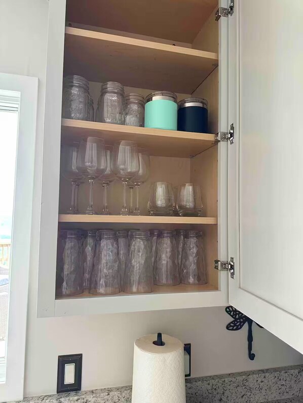 A kitchen cabinet with shelves holding glassware and jars.