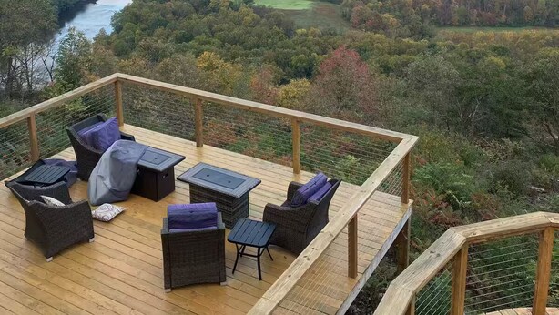 A wooden deck with wicker furniture overlooking a river and forested hills. - Our Shangri La (Berkeley Springs)