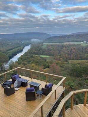 A wooden deck with wicker furniture overlooking a river and forested hills.