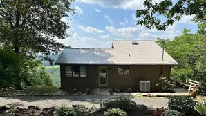 A single-story house with a metal roof, a front porch, and a gravel driveway. - Our Shangri La (Berkeley Springs)