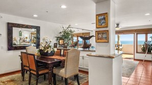 A spacious dining area with a wooden table and chairs, a large mirror, and a view of the ocean through large windows. - H1864: Remodeled 2Br villa, AC, 4-seat cart, OCEAN VIEWS, BBQ (Avalon)