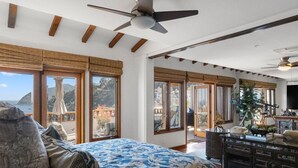 A spacious bedroom with a large bed, wooden beams, a ceiling fan, and a view of the outdoors. - H1864: Remodeled 2Br villa, AC, 4-seat cart, OCEAN VIEWS, BBQ (Avalon)