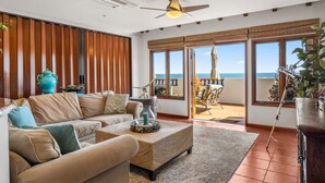 A spacious living room with a large sofa, a coffee table, and a view of the ocean through large windows. - H1864: Remodeled 2Br villa, AC, 4-seat cart, OCEAN VIEWS, BBQ (Avalon)