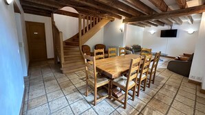 A dining area with a wooden table and chairs, a staircase, and a living room with a sofa and TV. - House by the river. Near Sarlat, Beynac, La Roque Gageac (Vézac)