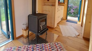 Tunnelmallinen mökin sisustus, jossa on puukamina, puiset hyllyt ja suuri ikkuna.