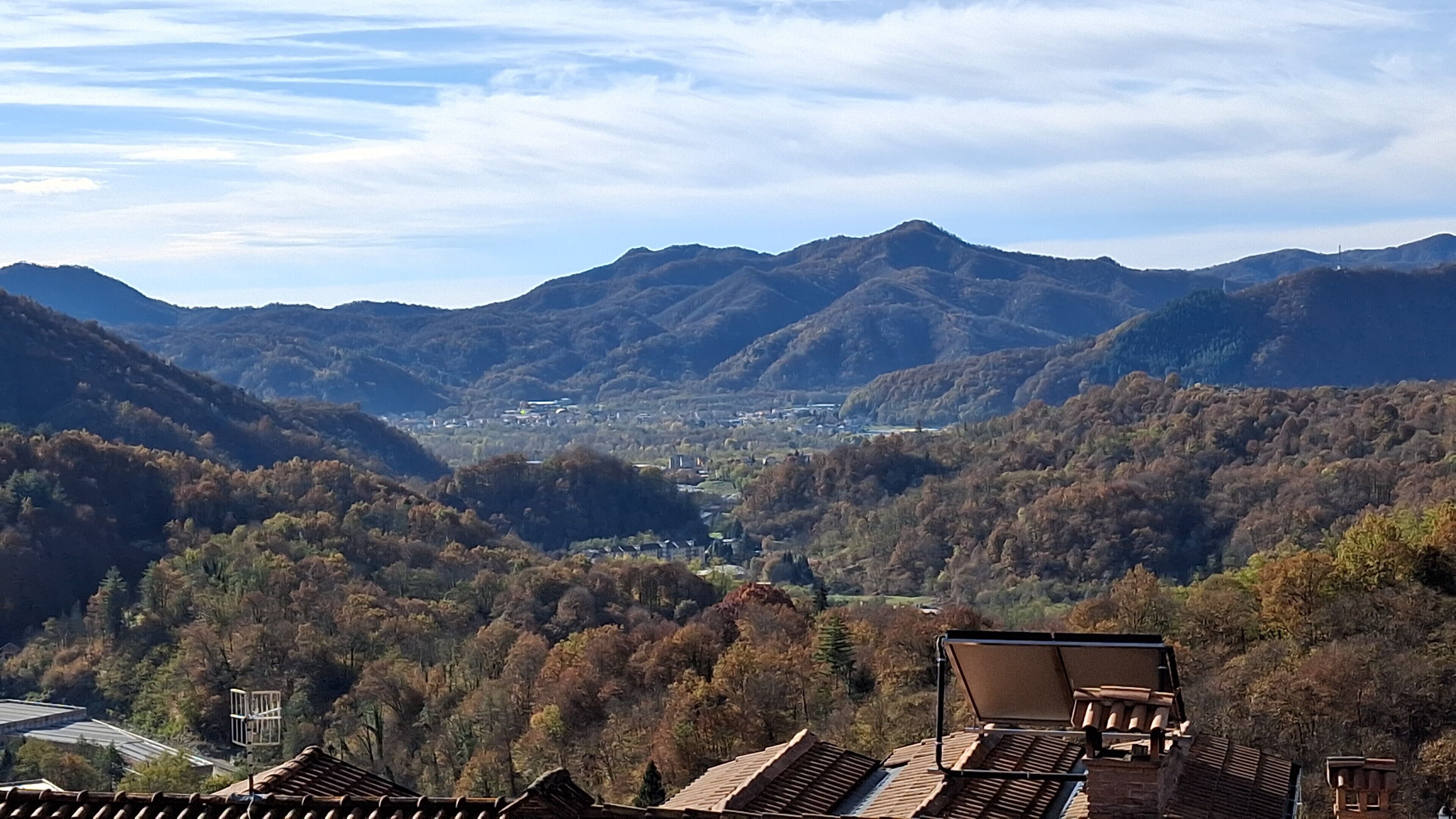 Eine Berglandschaft mit einem Tal, einer kleinen Stadt in der Ferne und traditionellen Ziegeldächern im Vordergrund.