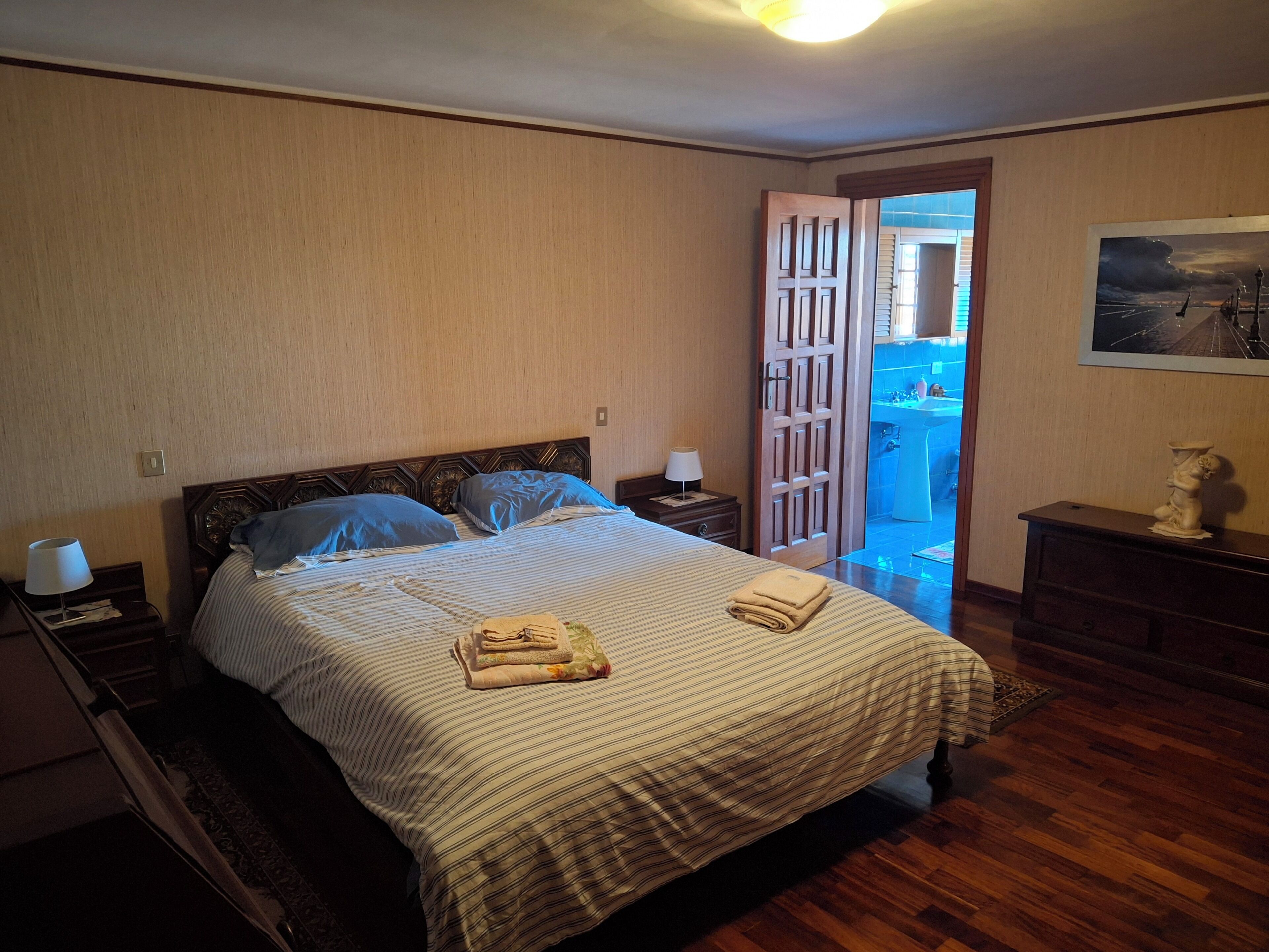 Une chambre à coucher comprenant un lit, une table de chevet, une commode, un tableau et une porte donnant sur un balcon.