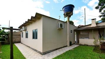 Un edificio pequeño de una sola planta con techo plano, un depósito de agua en el techo y un patio empedrado.