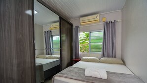 Une chambre avec un grand lit, un miroir, une fenêtre avec des rideaux et un appareil de climatisation.
