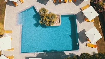 Luchtfoto van een rechthoekig zwembad omgeven door witte parasols en gele ligbedden.