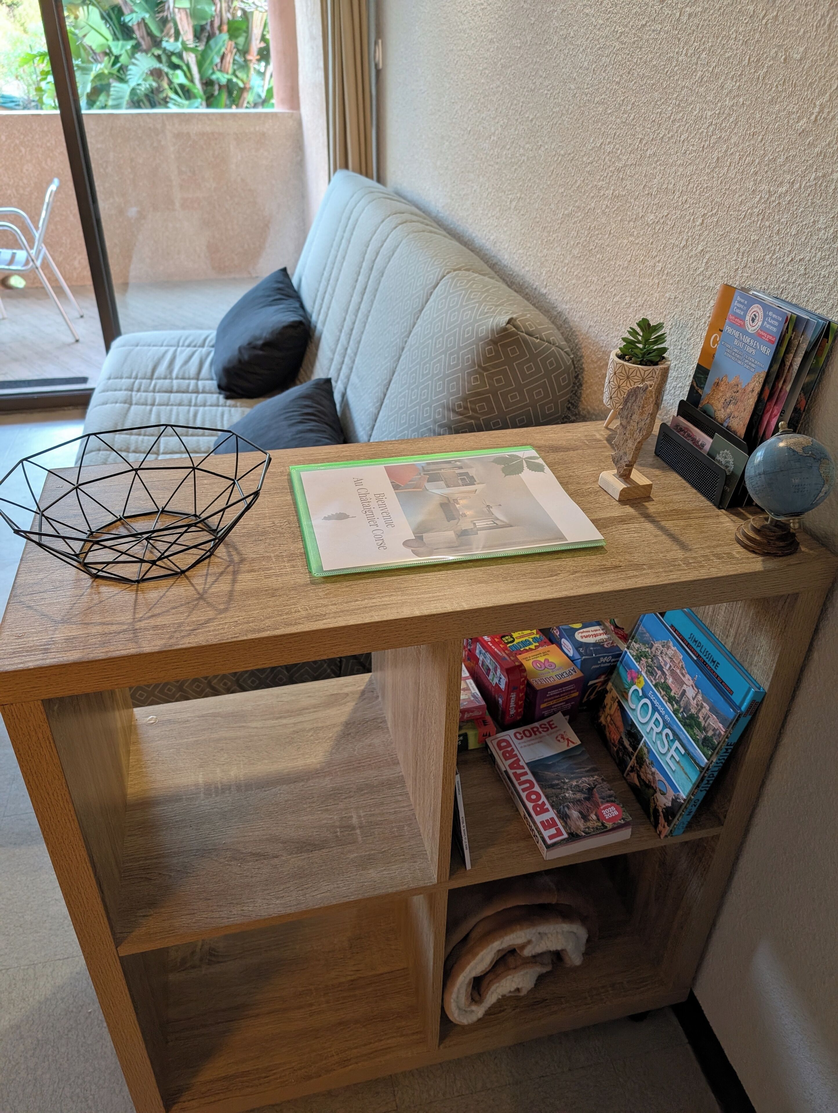 Une petite table d’appoint en bois, ornée d’un globe terrestre, d’une plante et d’une carte de bienvenue.