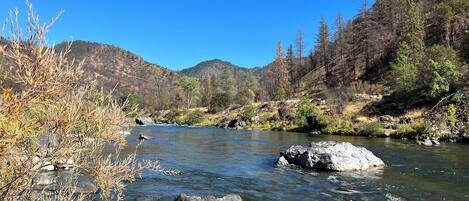 A clear river with rocks, surrounded by hills and sparse vegetation.