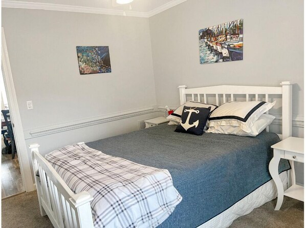 Une chambre à coucher avec un lit, une table de chevet, une chaise et deux tableaux accrochés au mur.
