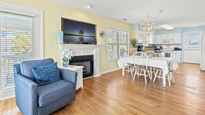 A spacious living room with a fireplace, a dining area, and a kitchen with white cabinets.