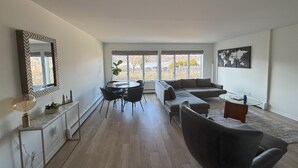 A spacious living area with a dining table, sofas, and a large window offering a view of the outdoors. - 2 Bedroom Condo -Views of West Point and Hudson River, steps from Metro North! (Garrison)