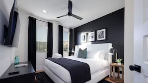 A modern bedroom with a white bed, black curtains, a ceiling fan, and framed pictures on the wall. - SIDE BY SIDE HOMES - 8 BEDROOMS- 2 HOT TUBS (Nashville)