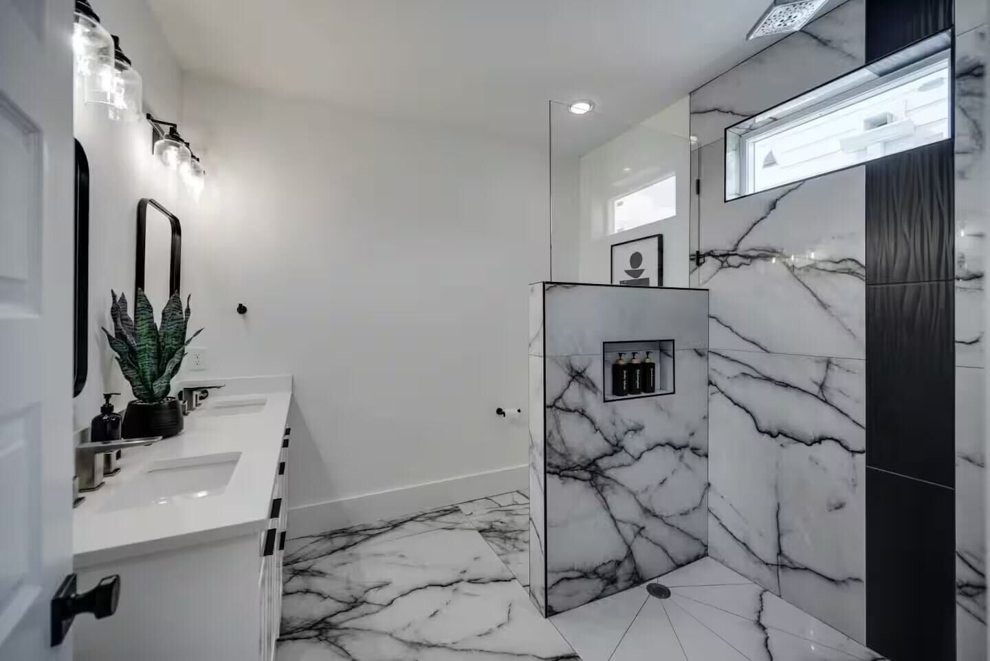 A modern bathroom with a white marble floor, a glass shower enclosure, and a vanity with a mirror and a potted plant.