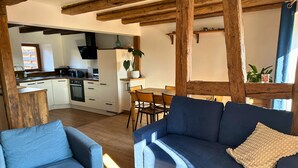 A cozy living room with a blue sofa, a wooden coffee table, and a dining area with a wooden table and chairs. - La P'tite Maison - Authentic stay on the Wine Route (Orschwihr)