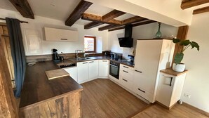 A modern kitchen with wooden beams, white cabinets, a built-in oven, and a sink. - La P'tite Maison - Authentic stay on the Wine Route (Orschwihr)