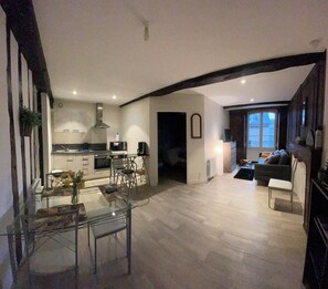 A modern kitchen with a dining area, a living room with a sofa and a small table, and a view of the outside through a window. - Charming Apartment in Dinan (Dinan)