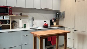 A modern kitchen with grey cabinets, a wooden table, and a red kettle.