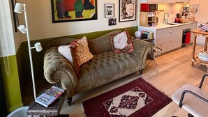 A cozy living room with a sofa, a coffee table, and a rug. There is a kitchen area with cabinets and a microwave.