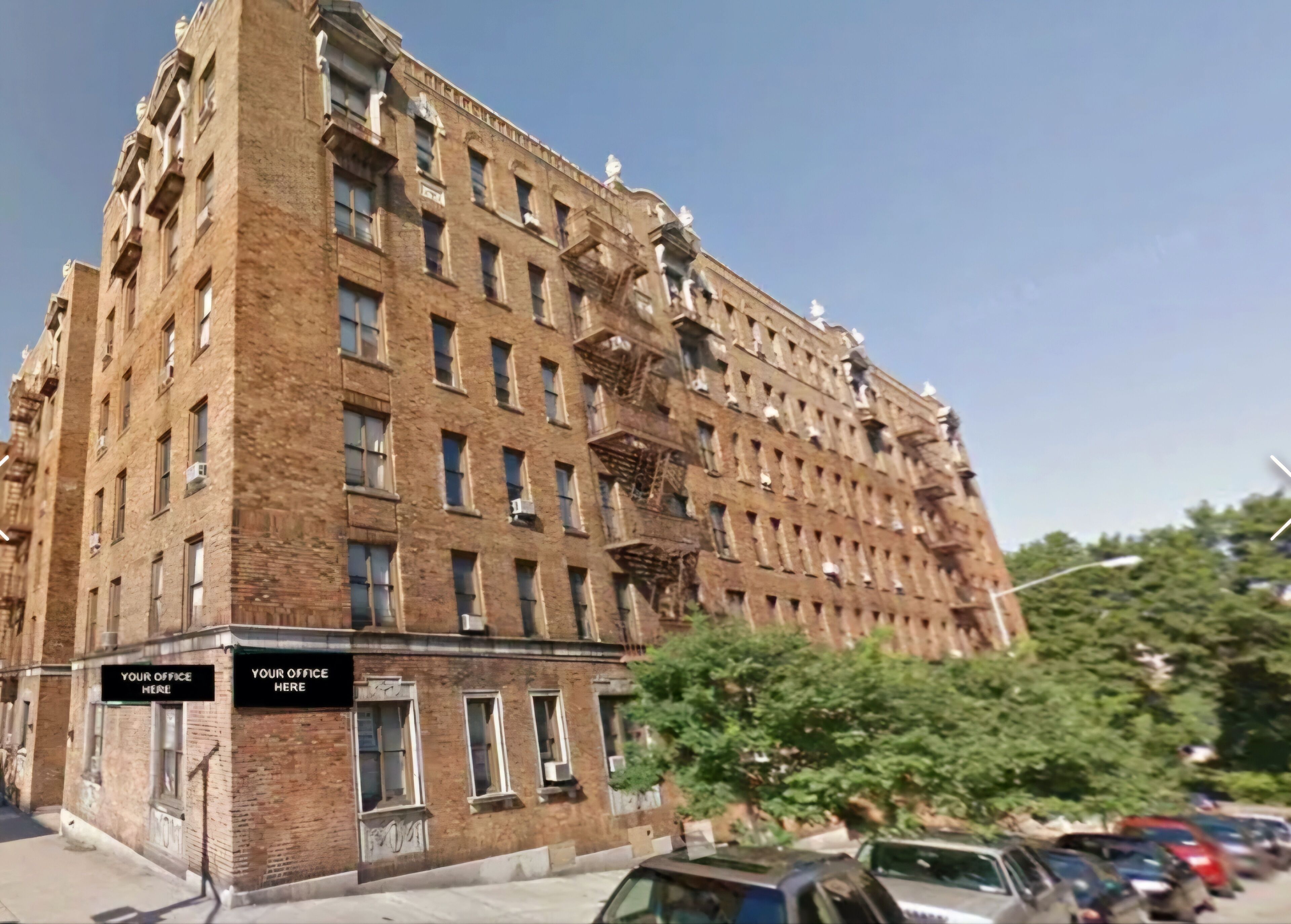 A large, multi-story brick building with multiple windows and balconies, some with air conditioning units. There are signs on the ground floor indicating office spaces.