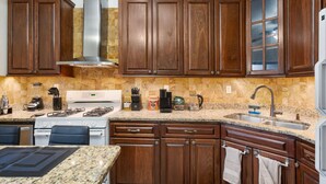 Una cocina con gabinetes de madera, encimeras de granito, estufa y pileta.