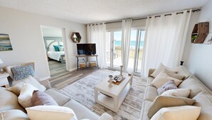 A spacious living room with a large sofa, a coffee table, and a TV. There is a balcony with a view of the sea. - Stunning 1st floor 2 bed w/beach service (Miramar Beach)