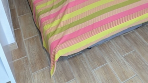 A bed with a wooden headboard, striped bedding, and a tiled floor. - Quiet apartment - furnished (Rouen)