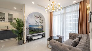 A modern living room with a flat-screen TV, a sofa, a coffee table, and a dining area with a kitchen in the background. - Vinhomes Central Park Landmark 81-Apts (Ho Chi Minh City)