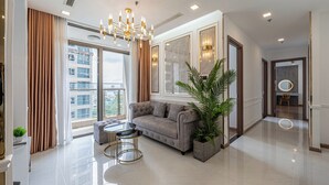 A modern living room with a sofa, two chairs, a chandelier, and a large window with curtains. - Vinhomes Central Park Landmark 81-Apts (Ho Chi Minh City)