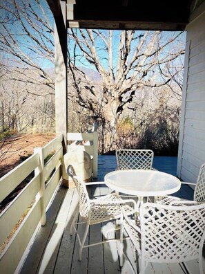 Un espace extérieur aménagé, abrité et doté d’une table ronde et de chaises blanches, offrant une vue sur un paysage verdoyant bordé d’arbres.