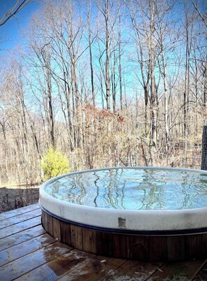Un bain à remous sur une terrasse en bois, avec une forêt en arrière-plan.