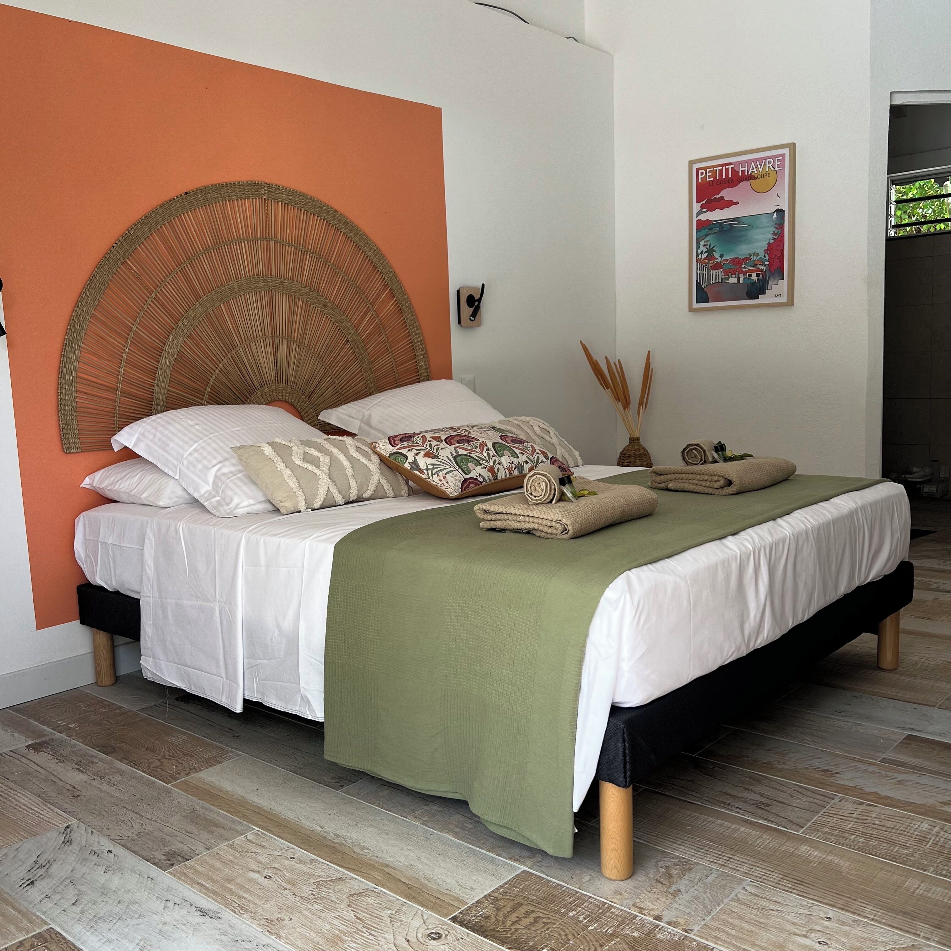 A bed with a woven headboard, white bedding, and a green throw blanket.