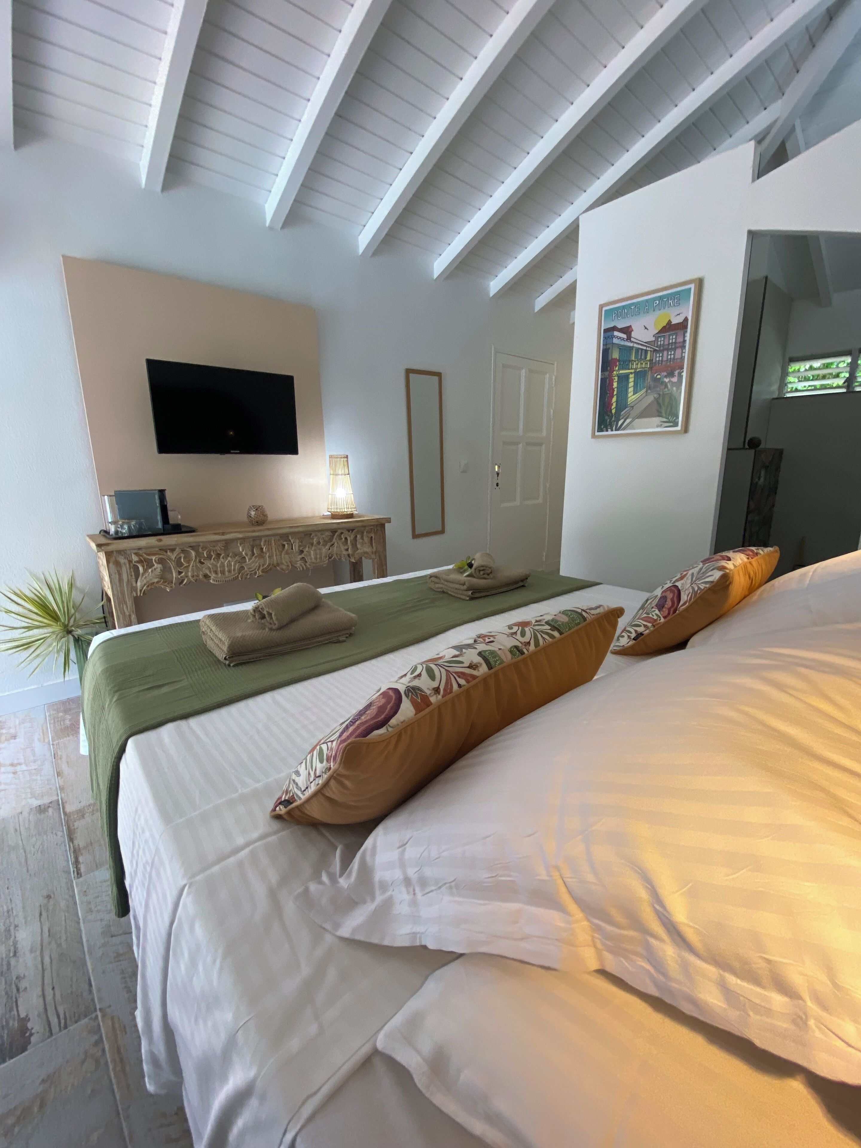 A hotel room with a bed, a flat-screen TV, a bedside table with a lamp, a framed picture on the wall, and a door.
