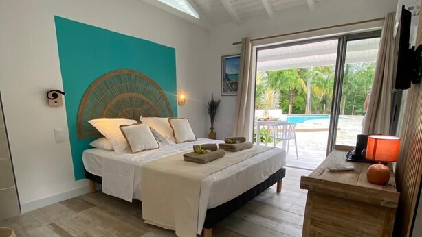 Une chambre spacieuse avec un grand lit, une commode en bois et une vue sur la piscine, accessible par une porte-fenêtre coulissante.