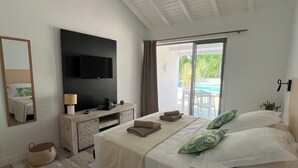 Une chambre spacieuse avec un grand lit, un téléviseur à écran plat fixé au mur, une commode en bois et une grande fenêtre donnant sur un paysage verdoyant.