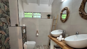 Une salle de bain moderne dotée d’une grande fenêtre, de deux lavabos, de toilettes et d’un espace douche.