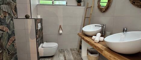 A modern bathroom with a large window, two sinks, a toilet, and a shower area.