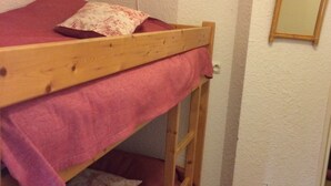 Ein Stockbett mit einer rosa Decke, einer Holzleiter, einer Wandlampe und einem Spiegel.
