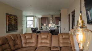 A modern living room with a brown leather sectional sofa, a dining area with a kitchen in the background, and a pendant light. - Apartment for 8 with terrace and BBQ in the city center (Arandas)