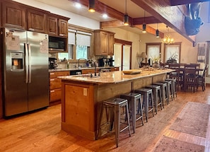 Una cocina amplia con una isla grande, electrodomésticos de acero inoxidable, gabinetes de madera y una zona de bar con taburetes.