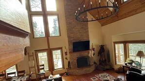 A spacious living room with a large black leather sectional sofa, a stone fireplace, and a high wooden ceiling with skylights. - Grinning Bear Lodge Luxury Cabin, Hot Tub, Massive Deck, Sleeps 14, Game Loft (Angel Fire)
