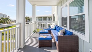A covered outdoor seating area with wicker furniture and blue cushions, overlooking a residential neighborhood. - Stay in this 3BR/2BA condo you may never want to leave! (Port Aransas)